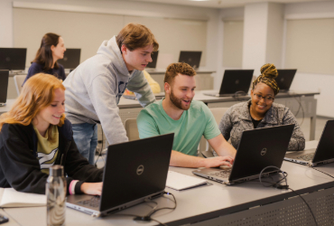 Young students gathered around looking at a laptop